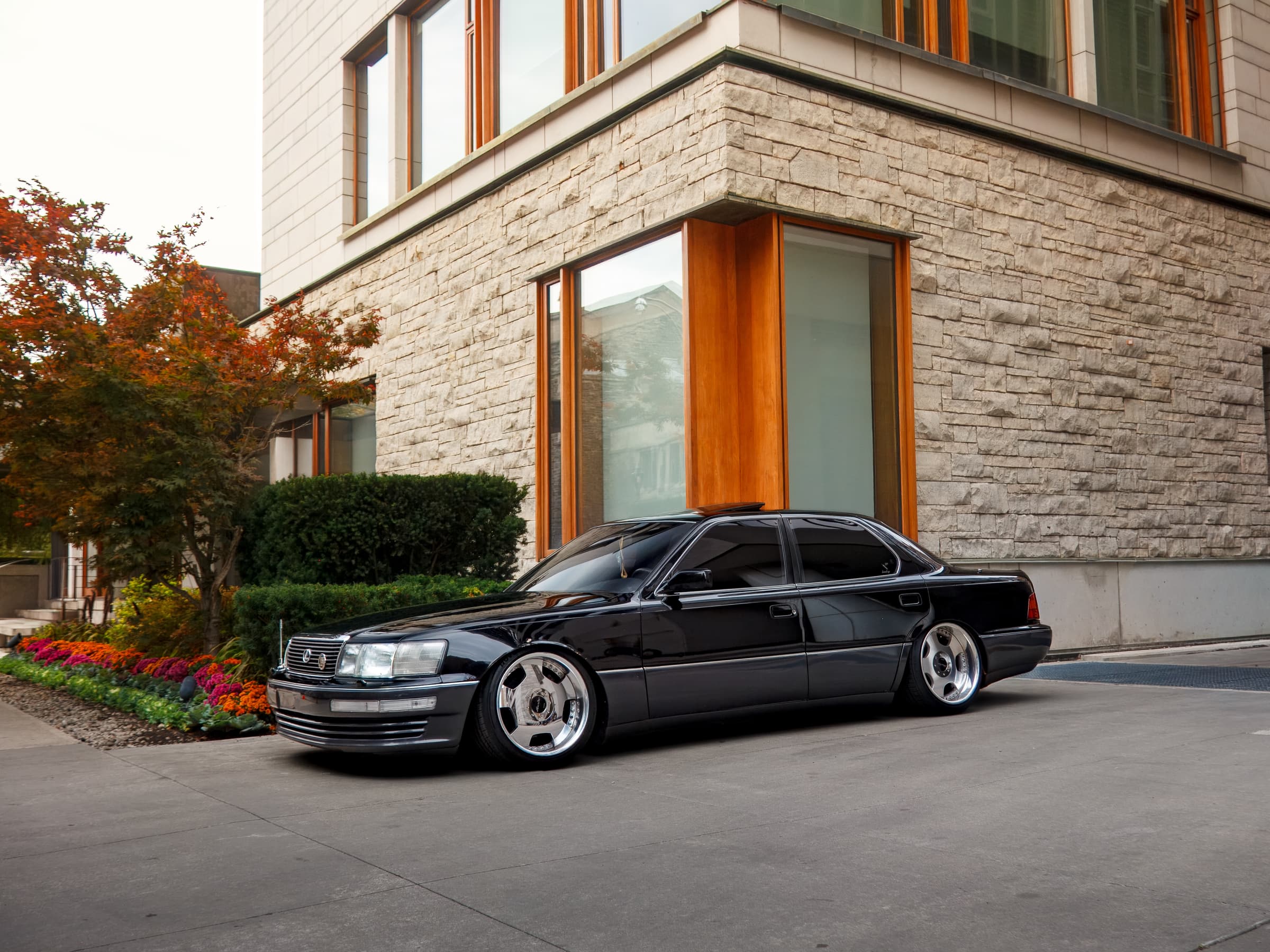 Black Lexus LS400 parked beside a stone facade and flower beds