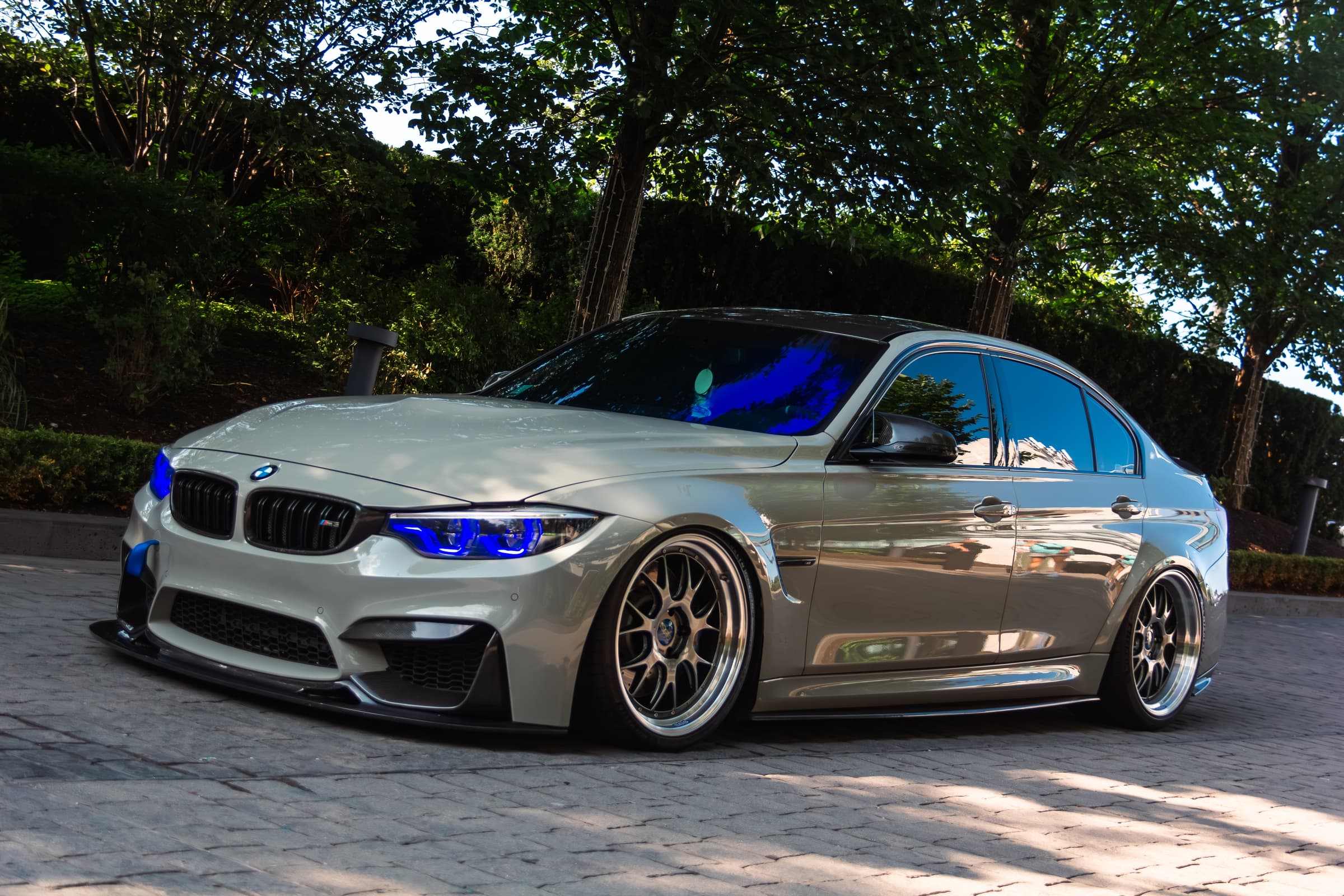 White BMW M3 with blue headlights parked in front of trees